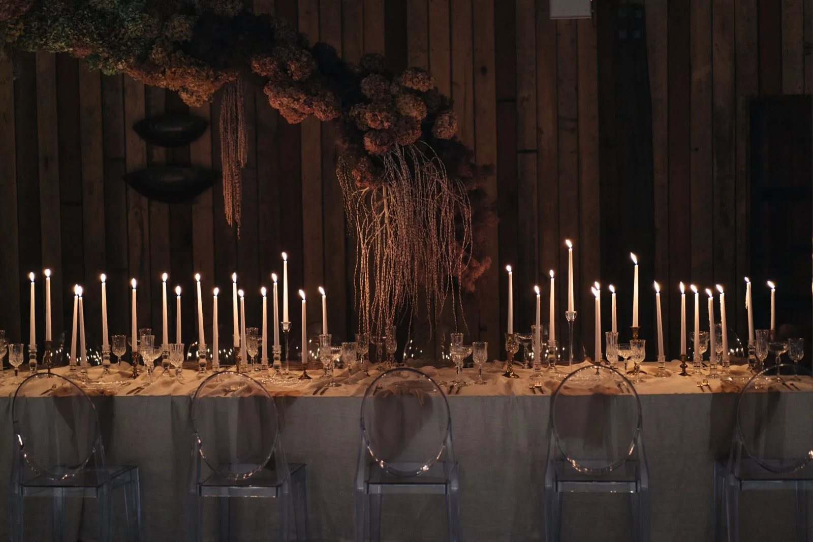 Dozens of tall candles along a long table against dark timber