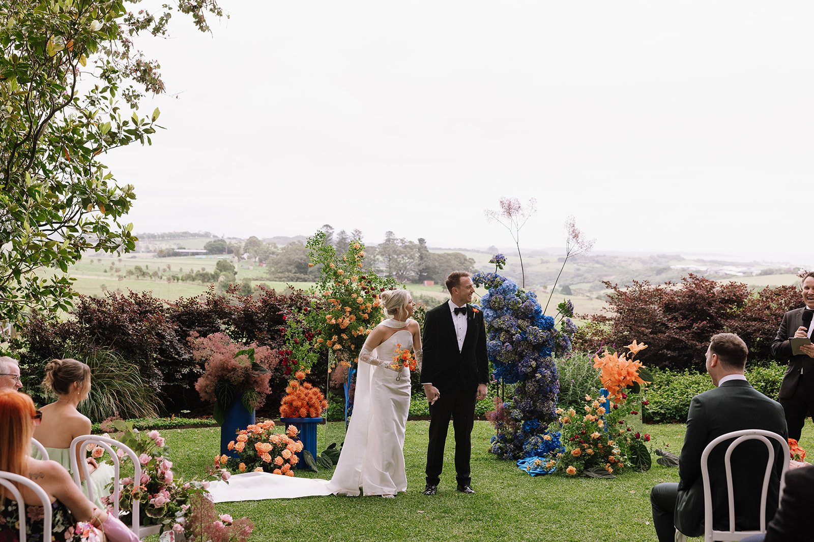 A ceremony on the lawn with bright florals, hills and the coast behind
