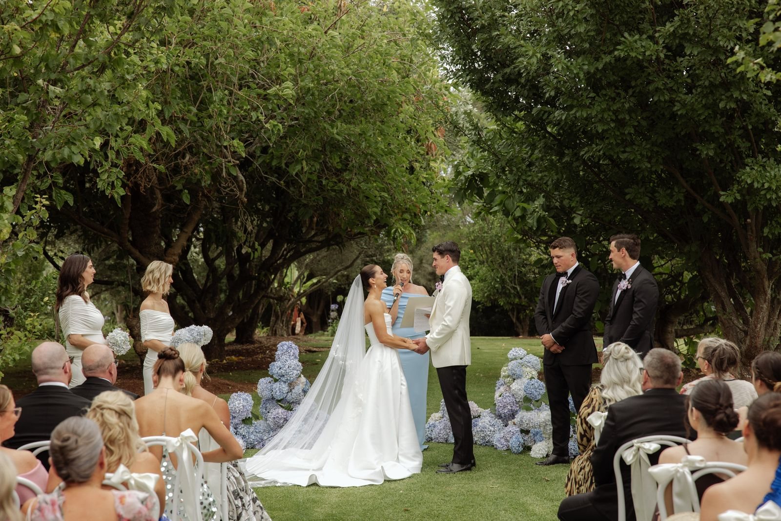 A garden ceremony with blue hydrangeas, the couple holding hands before their guests