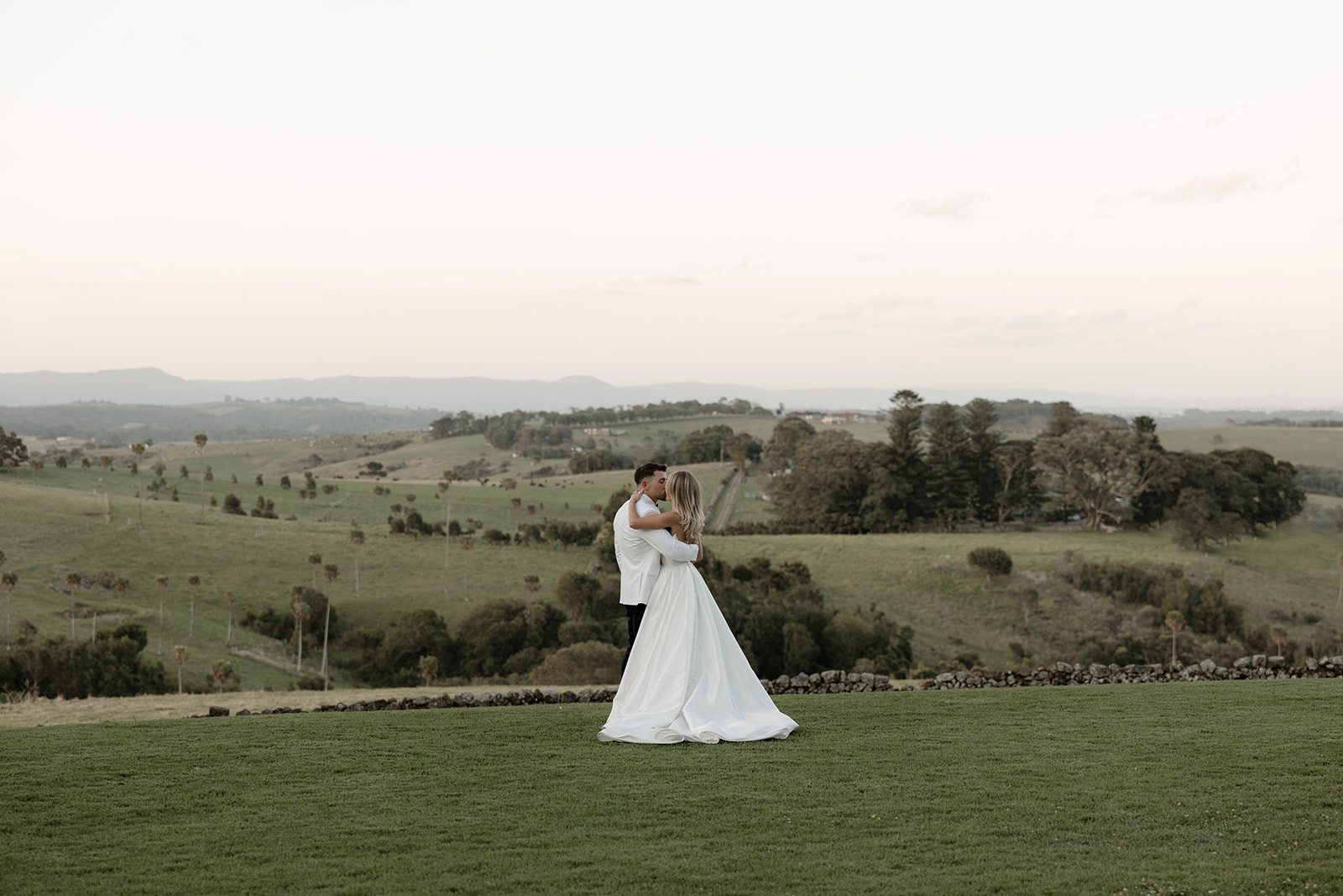 A couple embracing on a green hill, rolling farmland to the horizon
