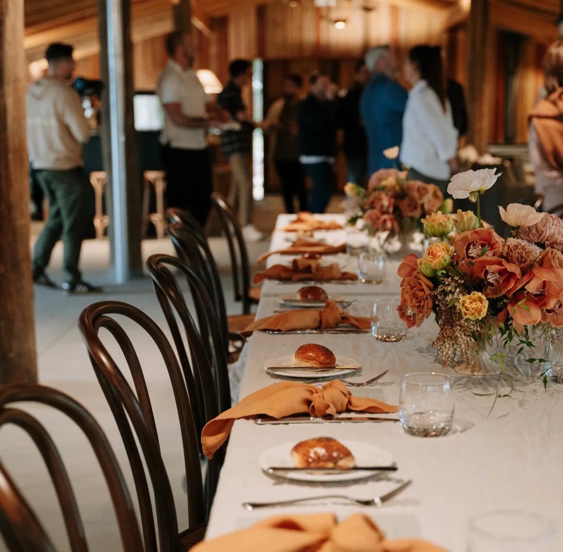 Guests at a long reception table set with orange napkins and florals